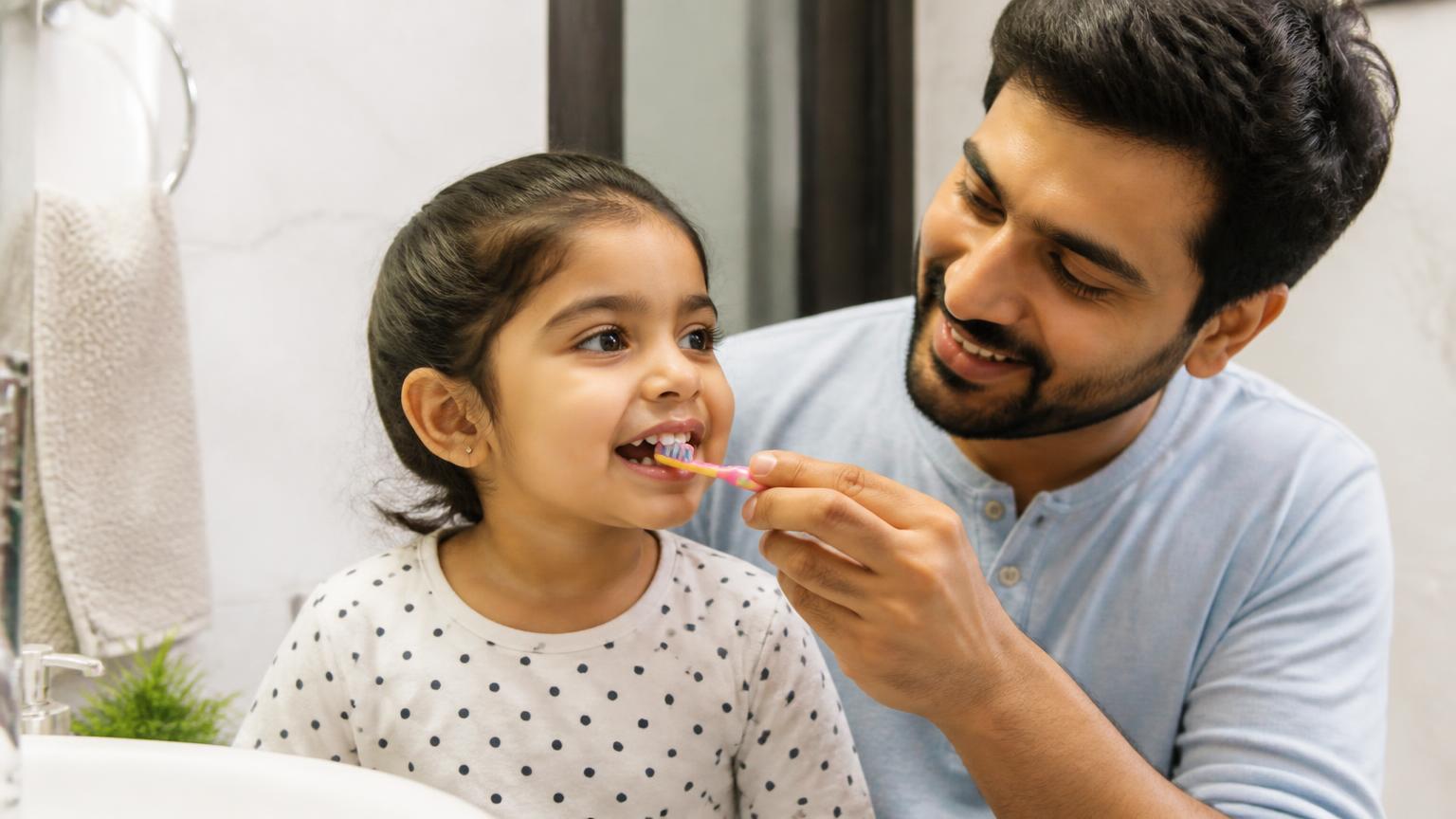 Parent helping a young child brush their teeth at home