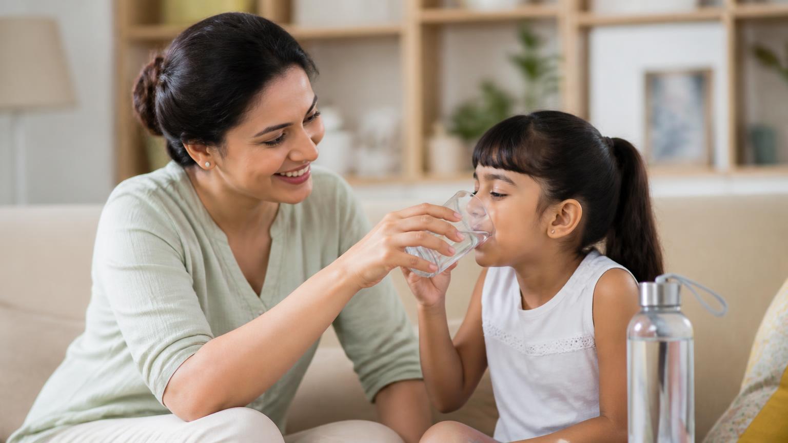 Parent offering a young child water instead of a sugary drink at home